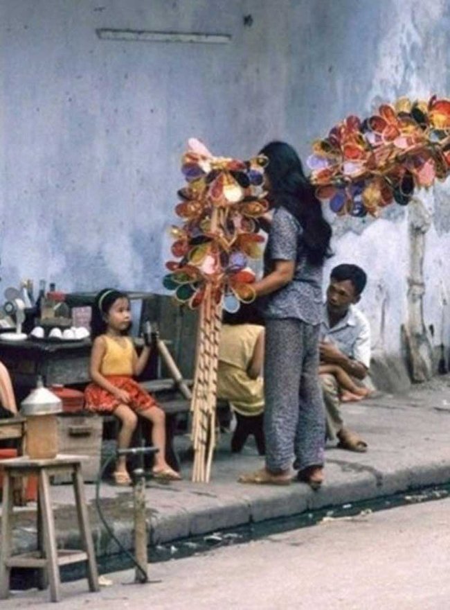 Hà Nội thập niên 1990, một cô bán đèn cù quay đang "chào hàng" với một bé gái bên quán nước.
