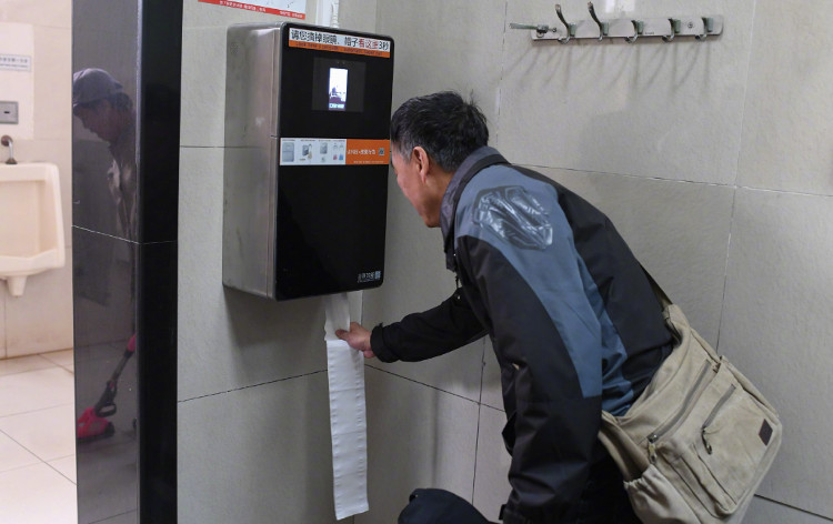 Một người đang lấy giấy vệ sinh từ chiếc máy thông minh có camera nhận diện khuôn mặt.