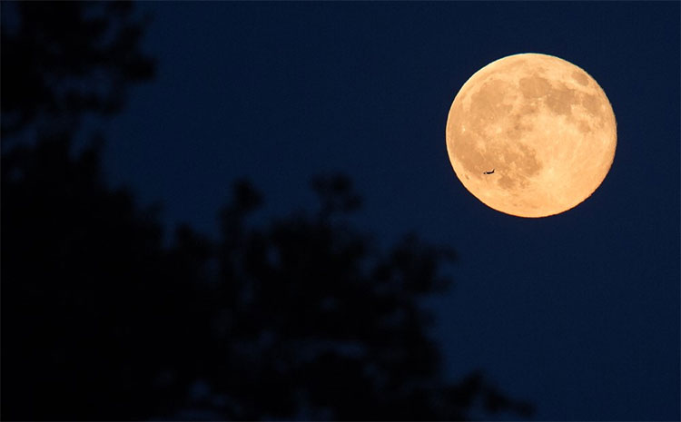 Một chiếc máy bay đang bay ngang qua phía trước Mặt Trăng trên bầu trời từ văn phòng của NASA ở Fort Myer Heights, Arlington, Virginia.